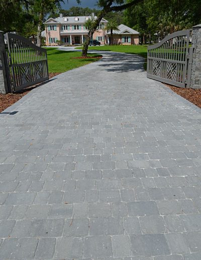 paver driveway winds through gates to a house in the distance