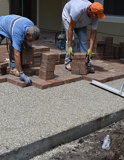 two workers lay pavers in a drive under construction