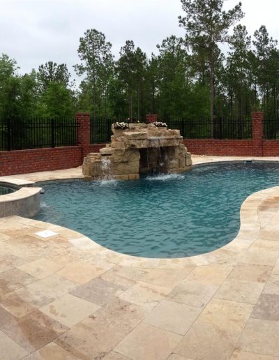 pool deck with a hot tub and rock waterfall feature