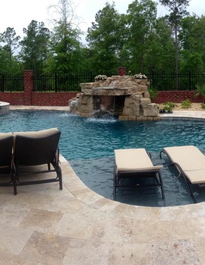 pool deck with a hot tub and rock waterfall feature