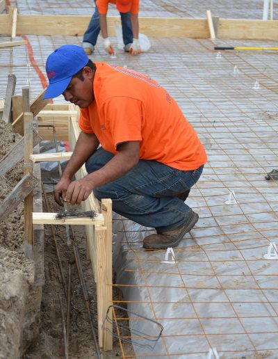 a man leans over to check his work on a concrete footing