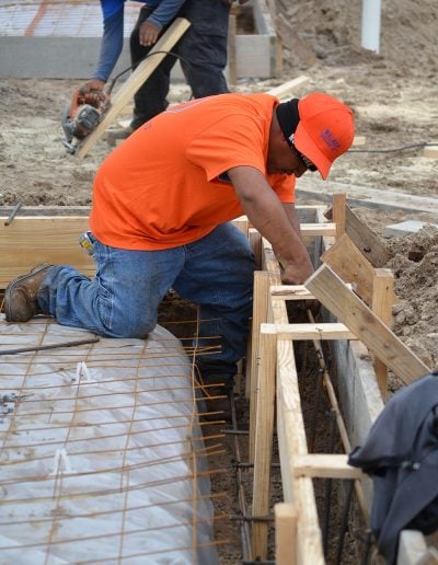 one worker cuts wood while another works with rebar